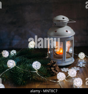 Gemütliche winter home. Laterne, Kerze, Girlande, Schneeflocken, Kegel, Zweig Weihnachtsbaum auf Holztisch. Die Atmosphäre der Märchen ist ein neues Jahr. Plac Stockfoto