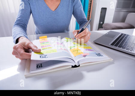 Nahaufnahme einer Frau schreiben Termine im Kalender Tagebuch auf weißem Schreibtisch Stockfoto