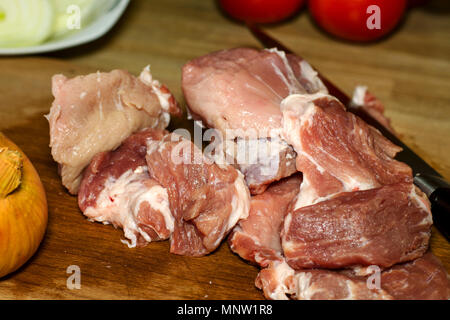 Rohes Fleisch. Rohen Rinderfilet Rind- oder Schweinefleisch, in große Stücke, Messer und Tomaten schneiden. Bereit für das Kochen. Liegt auf Holztisch. Close-up. Stockfoto