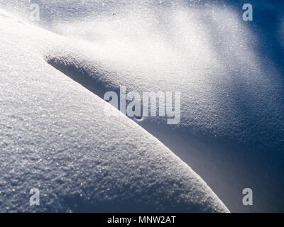 Snowdrift in der Sonne: eine tiefe Pulverschnee drift macht ein glattes Muster am frühen Morgen Sonnenschein. Stockfoto