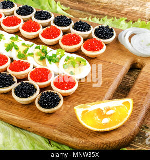 Hausgemachte Törtchen mit rotem Kaviar, Salat und Eier. Auf einem Schneidebrett. Mit Zwiebel und Zitrone. Konzept von Luxus essen. Platz. Close-up. Stockfoto