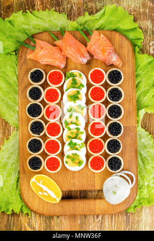 Hausgemachte Törtchen mit roter und schwarzer Kaviar, Lachs, Salat und Eier. Auf einem Schneidebrett. Konzept von Luxus essen. Startseite flache Ansicht. Vertikale. Close-up. Stockfoto