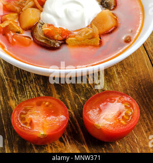 Hausgemachte rote Gemüsesuppe oder Borschtsch in die weiße Platte, Tomaten, Knoblauch, Brot und Speck. Auf einer hölzernen Hintergrund. Platz. Close-up. Stockfoto