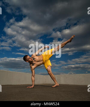 Austrickst, auf die Straße. Kampfsportarten Mann Kick mit Hand unterstützung barfuß. Bhudda Verkürzungen von unten gegen den Himmel. Stockfoto