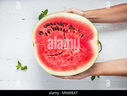Wassermelone in weibliche Hände auf einem Holztisch. Stockfoto