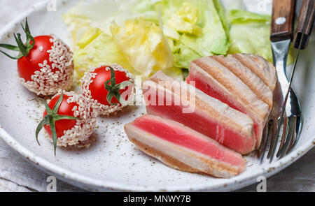 Gegrillter Thunfisch mit Spice, Kirschtomaten, Sesam und Salat in eine Platte auf dem Tisch. Gourmet Abendessen. Selektiver Fokus Stockfoto