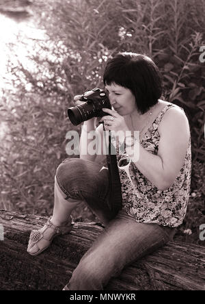 Fotografin in der Natur sitzen mit einer Kamera in den Händen und Bilder aufnehmen. Stockfoto