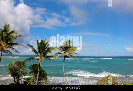 Ein voller Regenbogen begann in den Gewässern an der Ostküste von Kauai, Hawaii und da es immer größer und heller, es bewegte sich in Richtung Küste. Stockfoto