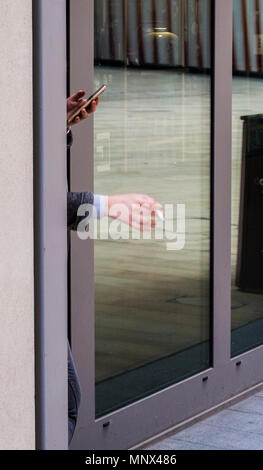 Die Frau Hände peering hinter einer Wand, eine Hand, die Zigarette, die anderen über ein Mobiltelefon, Kings Cross, London, England, Großbritannien Stockfoto