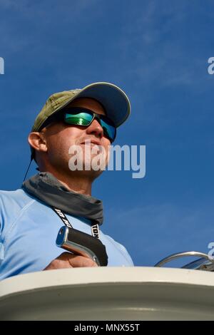 Kapitän am Rad des Fischerboot, das Tragen von reflektierenden Sonnenbrille und Kappe. Reflexion des Wassers und der Brücke in der Brille gesehen, Orange Beach, Alabama, USA. Stockfoto