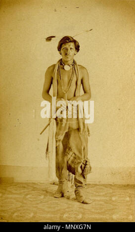 Porträt eines Native North American Man. Foto (schwarz und weiß) carte de visite; Studio Portrait of Native North American Man stehen, tragen zwei Adler Federn im Haar, ein dentalium Halskette, Halskette, ein zusätzliches Kleidungsstück mit einem Tuch um den Hals drapiert, ein paar Leggings, ein Bein Ornament auf seinem linken Knie, eine Decke um seine Taille gewickelt, ein paar Mokassins, und halten ein Tomahawk; Omaha (?), den Vereinigten Staaten von Amerika. 1860. 1148 Studio Portrait of Native North American Man Stockfoto