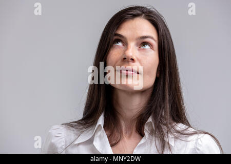 Attraktive Frau tief in Gedanken suchen, um sich mit einem nachdenklichen Ausdruck in einem Kopf und Schultern Portrait auf Grau Stockfoto