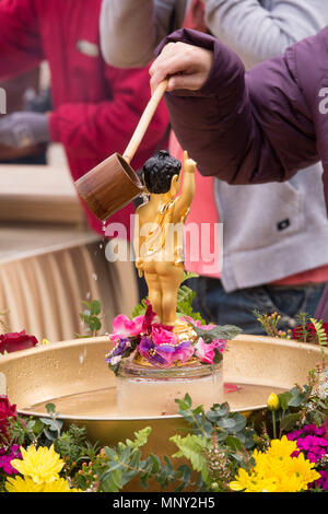 Nahaufnahme von Frau Gießen von Wasser aus einem kleinen hölzernen Löffel über die Schulter ein kleines Baby Buddha Figur, stehend auf einem bunten Lotus. Stockfoto