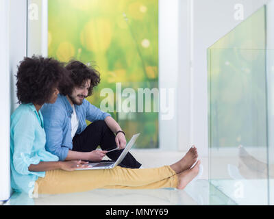 Junge schöne multiethnischen paar mit einem Laptop und Online-shopping auf dem Boden sitzend Stockfoto