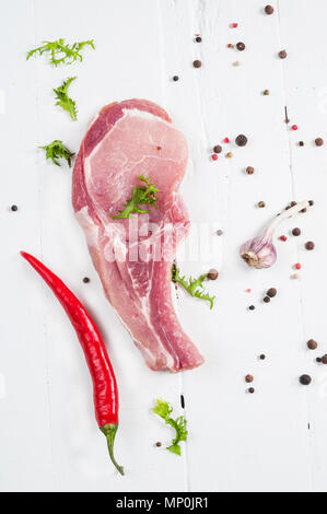 Ansicht von oben rohes Schweinefleisch Steak und Knoblauch fein hacken, Chilischote auf weißem Holz- Hintergrund. Stockfoto