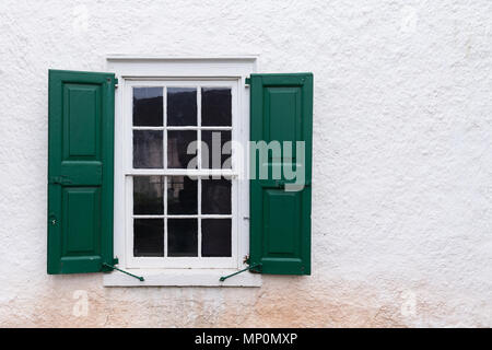 Alte Fenster mit grünen Fensterläden auf einer weißen Wand Stockfoto