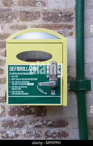 Automatisierter externer Defibrillator (AED). Notfall lebensrettende medizinische Ausrüstung in ein an der Wand montierter Schrank, in einem ländlichen Dorset Village entfernt. England. Stockfoto
