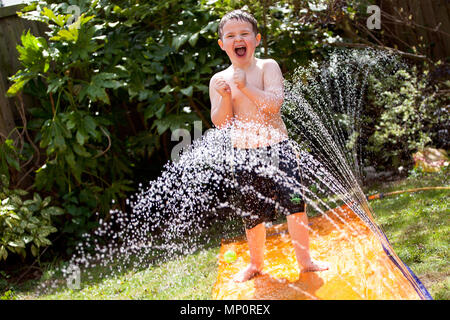 Jungen spielen mit Wasser Sprinkler im Garten auf der Rückseite Stockfoto