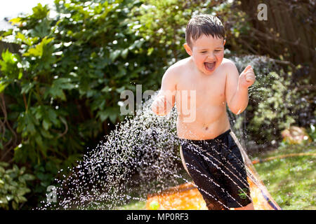 Jungen spielen mit Wasser Sprinkler im Garten auf der Rückseite Stockfoto