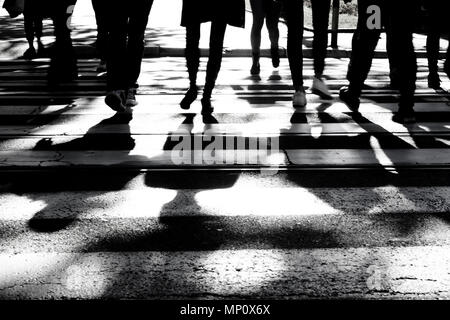 Verschwommene Silhouetten und Schatten der Menschen über die Straße am Zebrastreifen in Schwarz und Weiß, nur Beine, unkenntlich. Stockfoto