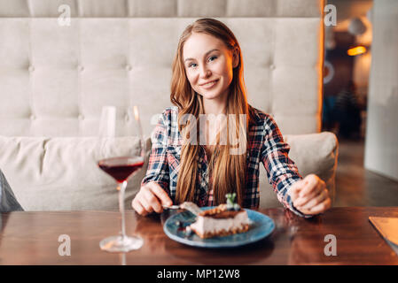 Porträt der jungen Frau im Cafe, süße Kuchen und Rotwein im Glas auf dem Tisch. Mädchen mit Schokolade Dessert im Restaurant Stockfoto