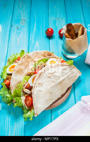 Pita sandwich gefüllt mit Huhn, Ei, Salat, Käse, Cherry Tomaten auf Blau Holz. Stockfoto