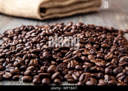 Stapel von gerösteten Kaffeebohnen auf einem Holztisch mit hessain Sack im Hintergrund Stockfoto