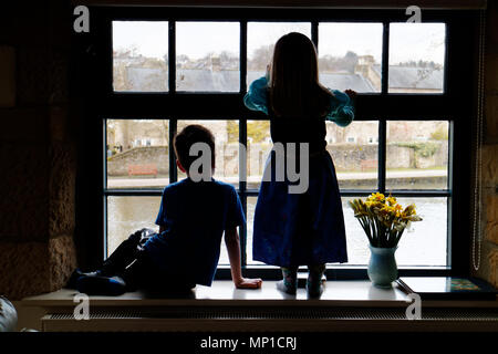 Bruder (5 Jahre alt) und Schwester (3 Jahre alt) saß auf dem Fensterbrett, gegen ein Schiebefenster mit dem Fluss Wye in Bakewell außerhalb Silhouette Stockfoto