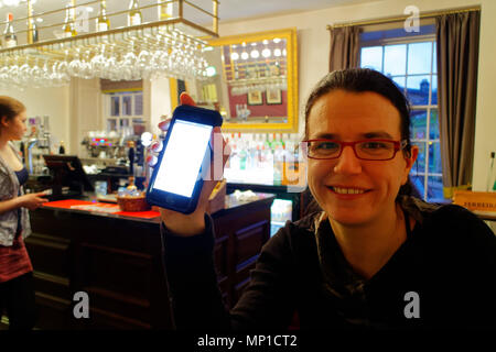 Eine junge Frau, die immer gute Nachrichten auf ihrem iphone in der Bar des Rutland Arms in Bakewell, England Stockfoto