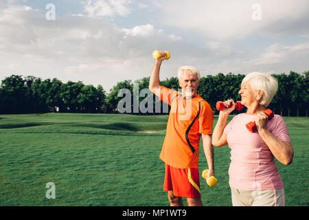 Älterer Mann und Frau arbeiten mit Hanteln in einem Park an einem sonnigen Tag Stockfoto