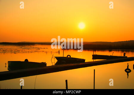 Den Sonnenuntergang von einem kleinen Dock mit altem Holz Fischerboote und Reed in der Ferne. Gelassenheit. Stockfoto