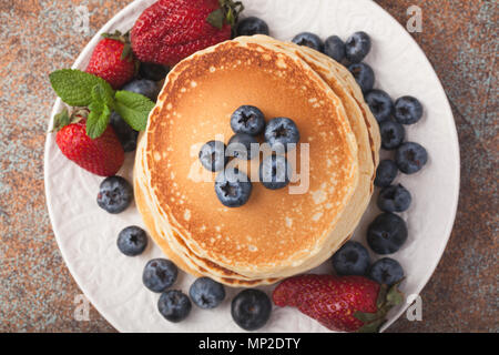 Close-up leckere Pfannkuchen mit frischen Heidelbeeren, Erdbeeren und Ahornsirup auf einem rostigen Hintergrund. Stockfoto