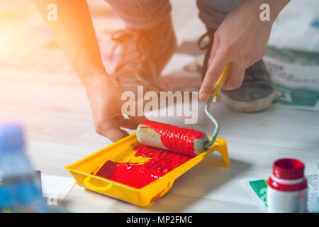 Eine Nahaufnahme einer Frau in Jeans und Turnschuhe zieht rote Farbe mit einer Rolle in einem Fach der Maler für die Wände zu Rep bereitet Stockfoto