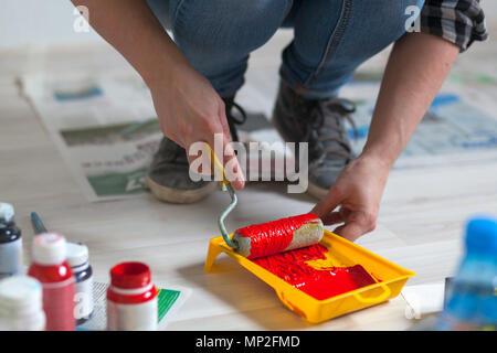 Eine Nahaufnahme einer Frau in Jeans und Turnschuhe zieht rote Farbe mit einer Rolle in einem Fach der Maler bereitet sich auf die Wände zu re Stockfoto