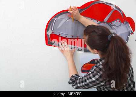 Eine Nahaufnahme einer weiblichen Künstlerin zeichnet ein Bild von einem Auto und zieht es in Rot auf einer weißen Wand im Kinderzimmer Stockfoto