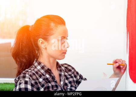 Nahaufnahme einer Künstlerin in schwarzen und weißen Hemd zeichnet ein rotes Auto an der Wand mit einem Bleistift auf eine weiße Wand im Kinderzimmer Stockfoto