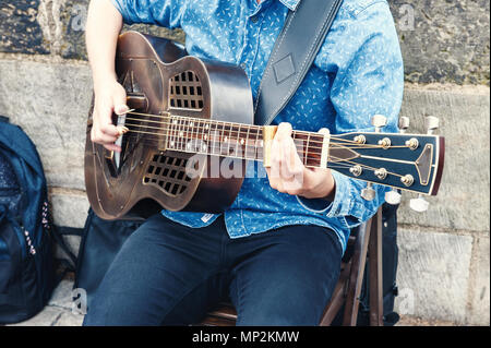 Ein Mann Gitarre spielen sitzen auf der Straße während des Tages. Stockfoto