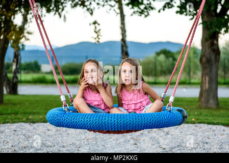 Zwilling Mädchen auf Spinnennetz nest Schaukel auf dem Spielplatz. Aktive Kinder spielen mit Giant Swing-N-Folie Monster Web Schwingen am Spielplatz im Freien Stockfoto