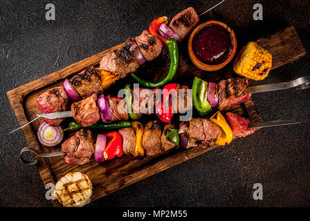 Frisch - auf dem Grill Feuer Fleisch Rindfleisch Shish Kebab mit Gemüse und Gewürzen gekocht, mit Barbecue Sauce und Ketchup, auf einem dunklen Hintergrund auf einem Holz Stockfoto