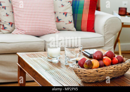 Detail aus einem Wohnzimmer Innenraum, englischer Landhausstil mit zwei Sitzen Sofa mit Kissen, eine hölzerne alte Couchtisch mit Brille und einem Korb mit einer Stockfotografie