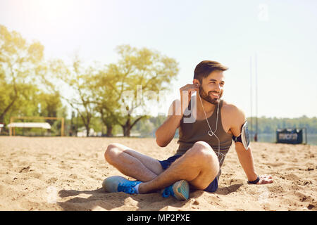 Ein bärtiger Sportsman sitzt auf dem Sand am Strand. Stockfoto
