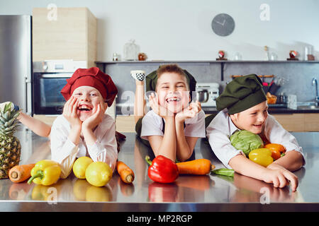 Lustige Kinder in der Uniform der Köche auf dem Tisch in pflanzlichen Stockfoto