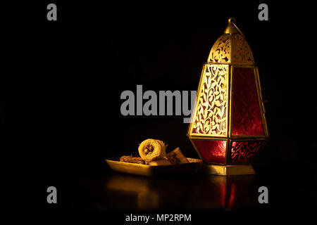 Traditionelle ornamentale arabische Laterne mit einer brennenden Kerze in einem dunklen Studio Einstellung mit traditionellen arabischen Süßigkeiten. Festivel Grußkarte für Ramadan Stockfoto