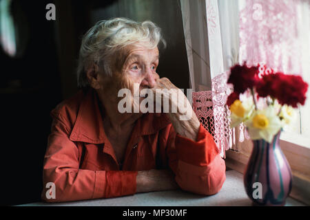 Ältere Frau sieht traurig aus dem Fenster. Stockfoto