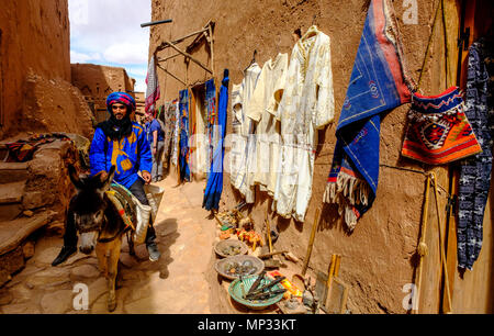 Ein lokaler Mann in traditioneller Tracht reitet ein Esel Vergangenheit Waren zum Verkauf in einem Stall in Aït Benhaddou, Marokko. Stockfoto