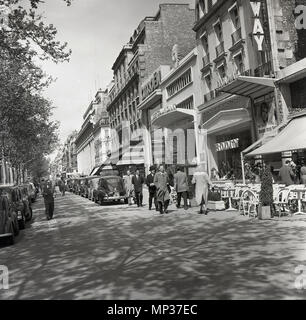 1950, Paris und einen Blick auf den Bürgersteig mit parkenden Autos bside Geschäfte und Cafés entlang der Avenue des Champs-Elysees, zeigt die französische Marken von Citreon, Rodin und die Broadway Kino, Stockfoto