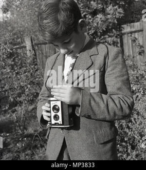 1950, historische, Teenager Schüler außerhalb in einem Garten mit einer Kodak "Brownie" Reflex Film Kamera. Diese Kamera wurde in England von Kodak Ltd. von 1946 bis 1960 gemacht. Wie man sehen kann, es zu benutzen, man schaute auf den Sucher und hielt die Kamera auf Höhe der Taille. Stockfoto