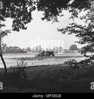 60er Jahre, England, Landwirt auf seinem Traktor ordentlich Pflügen eines Feldes. Stockfoto