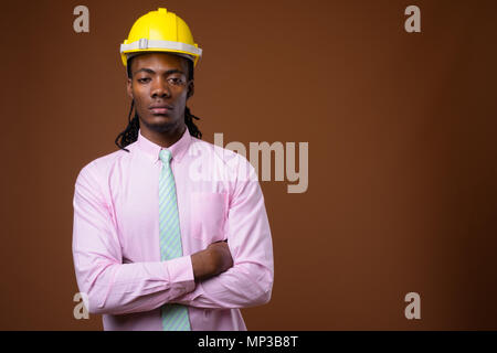 Jungen schönen afrikanischen Geschäftsmann mit hardhat gegen Braune ba Stockfoto