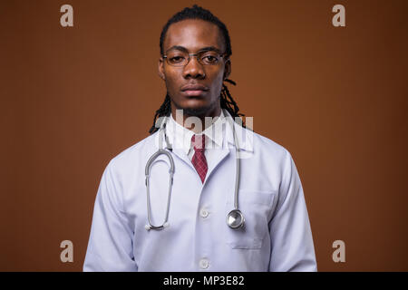 Junge schöne afrikanischer Mann Arzt gegen braunen Hintergrund Stockfoto